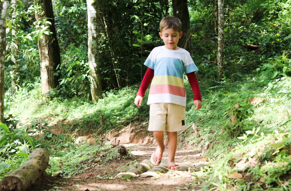 Criança caminhando em trilha na floresta, imagem ilustrativa para passeios em família em Monte Verde